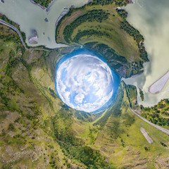 360 degree panoramic image of an abstract world turned inside out with green meadows around an oval sky with clouds