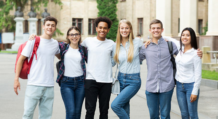 Classmates posing in front of university and smiling to camera