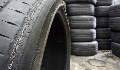 Irregular Tire Wear , Damaged black tire of side wear area on blurred pile old tyres background.
