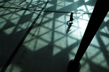 silhouette of a woman walking in shadows cast by sunlight coming through a moder glass roof. Top...