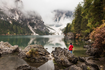 Women with red rain jacket enjoying the peaceful mystic view of a mountain lake with cloudy...
