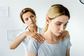 selective focus of chiropractor touching shoulders of attractive patient in grey t-shirt