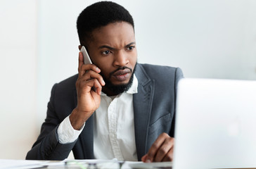 Serious businessman talking on phone and using laptop in office