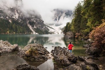 Women with red rain jacket enjoying the peaceful mystic view of a mountain lake with cloudy...