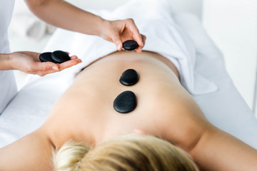 cropped view of masseur doing hot stone massage to woman in spa