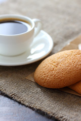 Oatmeal cookies, coffee mug and saucer on burlap tablecloth.