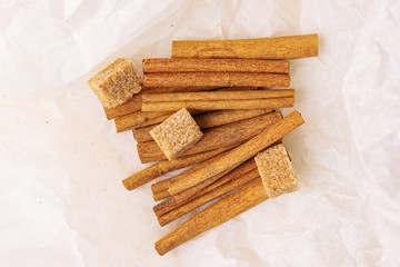 Cinnamon sticks and cane sugar on beige paper close-up. The concept of spices for baking, drinks and other dishes. Minimalism, place for text.