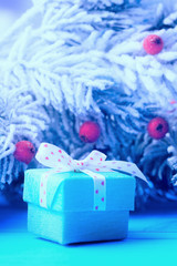 Gift box over frosty Christmas tree branches, blue tinted image