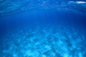 Underwater background of clear blue water on sandy sea floor