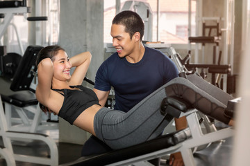 Obraz premium Young Asian woman in sportswear training sit up with male trainer at fitness gym.