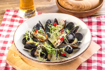 Cooked fresh mussels on white plate with glass of beer on wooden table