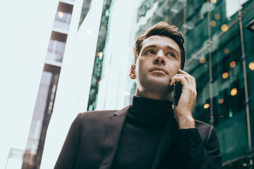 Attractive young stylish man on a phone in urban business background 