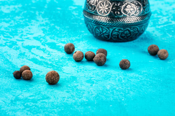 Allspice, Jamaica pepper. Scattered peppercorns with a vintage pepper mill, close-up on a teal blue...