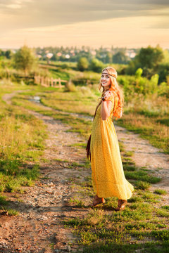 Happy girl in bohemian style yellow dress with guitar on the field turned back at sunset
