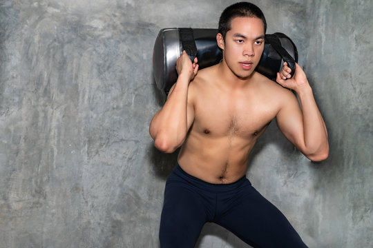 Perfect athletic Asian man training with power bag at gym.
