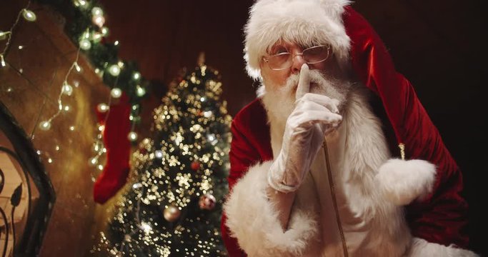Senior man in santa clause costume leaving christmas presents in boxes near fireplace and christmas tree - christmas spirit, traditions concept 4k footage