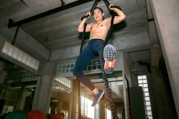 Crossfit athletic Asian man training rope climbing exercise at gym.