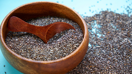 Nutritious chia seeds on a blue background. chia seeds in bowl and a spoon on kitchen table top view. Healthy and diet superfood product.