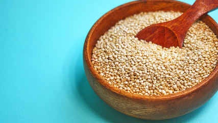 White quinoa seeds on a blue background. quinoa in bowl and a spoon on kitchen table top view. Healthy and diet superfood product.