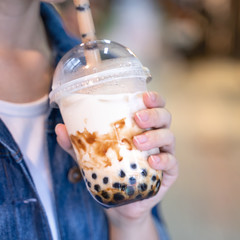 Young woman is holding, drinking brown sugar flavored tapioca pearl bubble milk tea with glass...