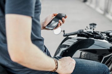 Close up of biker holding mobile phone while sitting on motorcycle.