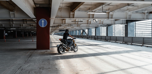 Distant plan of biker riding motorcycle at parking. Urban background.
