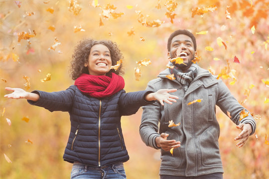 Happy afro couple throwing autumn fall leaves