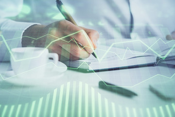 Double exposure of man's hands writing notes of stock market with forex chart.
