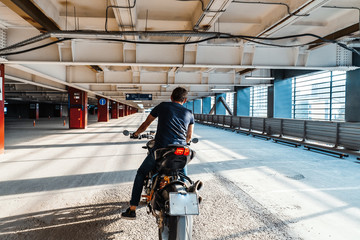 Distant plan of biker riding motorcycle at parking. Urban background.