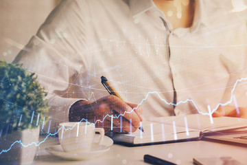 Double exposure of man's hands writing notes of stock market with forex chart.