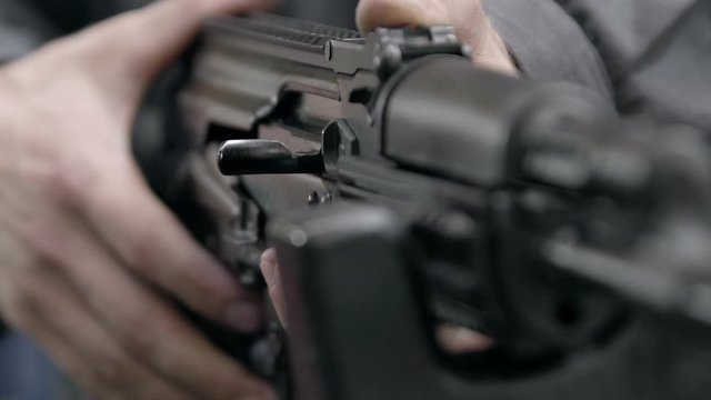 Slow motion charging rifle. Unlocking assault rifle. AK47 loading. Factory worker hand charging machine gun. Factory worker uniforms collects the AK-47