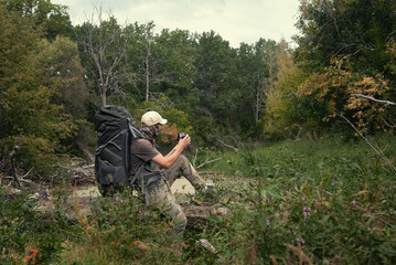 Tourist with large backpack in wilds early autumn photographs nature. Landscape with taiga forest, swamp. Hard hike walk