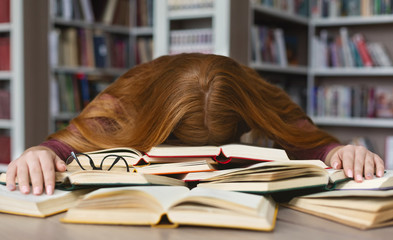 Tired redhead girl sleeping on books at campus library
