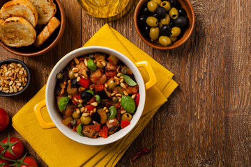 Traditional Italian caponata, served with croutons in a yellow, sunny pot. Decorated with basil and...