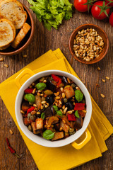 Traditional Italian caponata, served with croutons in a yellow, sunny pot. Decorated with basil and pine nuts.
