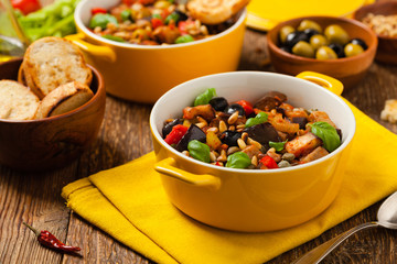 Traditional Italian caponata, served with croutons in a yellow, sunny pot. Decorated with basil and pine nuts.