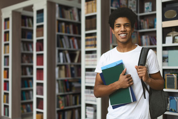 Fototapeta Handsome afro student posing on bookshelves background obraz