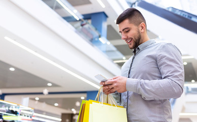 Handsome man using phone, shopping in mall