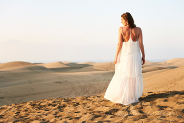 Fototapeta na wymiar Stunning girl in white dress standing in sand dunes