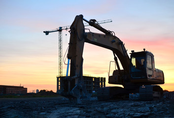 Large tracked excavator with hydraulic shears on a construction site against the background of the awesome sunset. Road repair, asphalt replacement. Small roughness sharpness, possible granularity