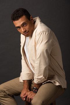 handsome mixed race man in beige shirt sitting on chair on black background