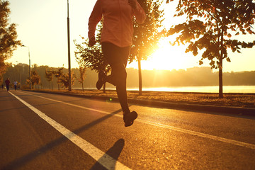 Runner runs on the road in the sun at sunset in an autumn park.
