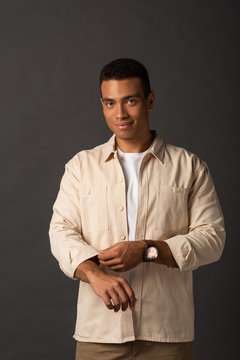 smiling handsome mixed race man in beige shirt on black background