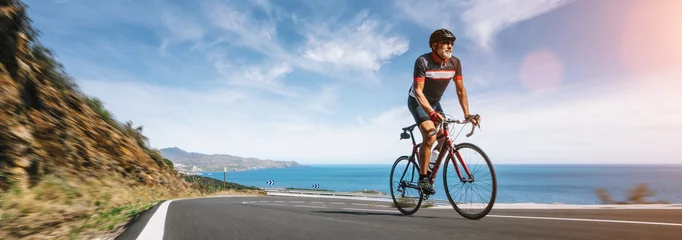 Fototapeten Mature Adult on a racing bike climbing the hill at mediterranean sea landscape coastal road © AA+W