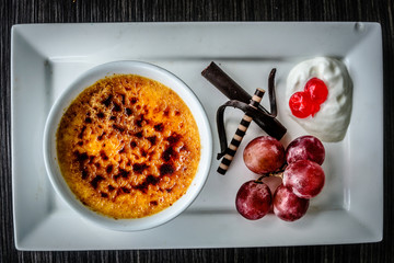 creme brulee dessert served with fresh cream, sweetened cherries, chocolate and grapes