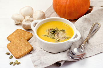 Bowl of Tasty Homemade Pumpkin Cream Soup decotated with Mushrooms and Pumpkin Seeds White Wooden Background Galette Horizontal