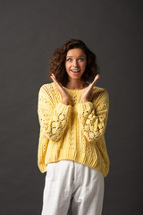 excited curly woman in yellow knitted sweater on black background