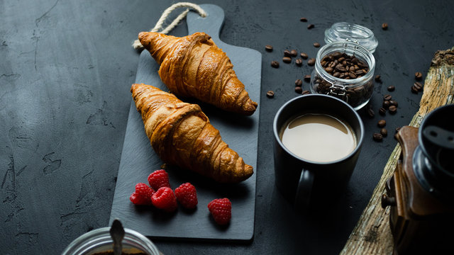 Croissant z malinami leżący na kamiennej desce. Ciemne tło, widok z g&oacute;ry.
