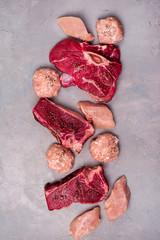 Three Pieces of Raw Fresh Beef Meat Steak Raw Chicken and Raw Chicken Cutlets on Gray Background Vertical Top View