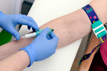 A nurse at the clinic introduces a catheter into a vein for a patient’s blood test. Hands of a...